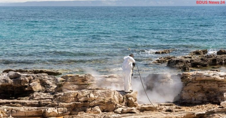 Person in white protective suit pressure washing rocks on the coast