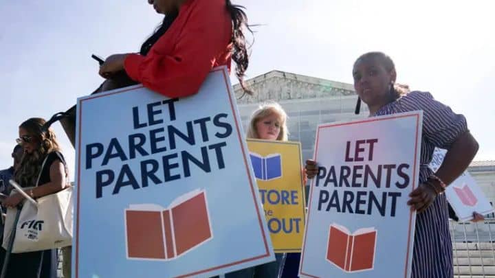 Demonstrators holding signs that read 'Let Parents Parent' during a protest regarding parental rights and school district policies, covered by BDUS News 24.